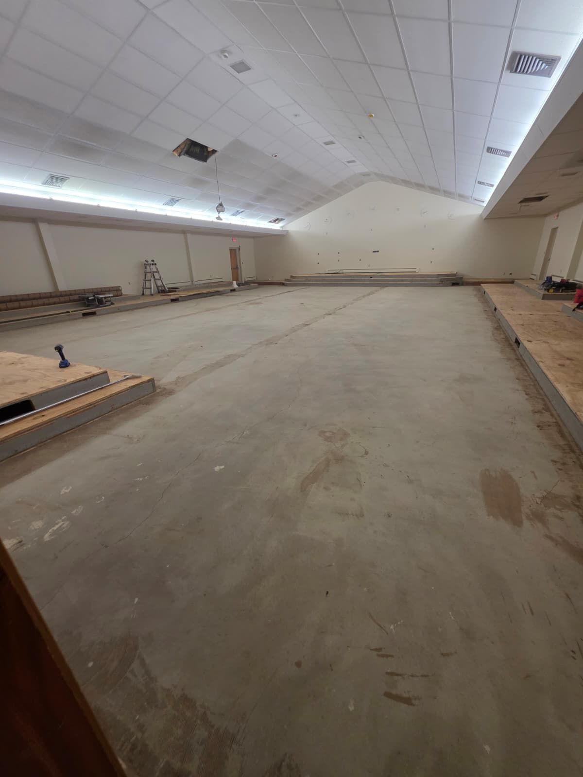Large empty warehouse-like room with a concrete floor and sloped white ceiling, under construction or renovation.