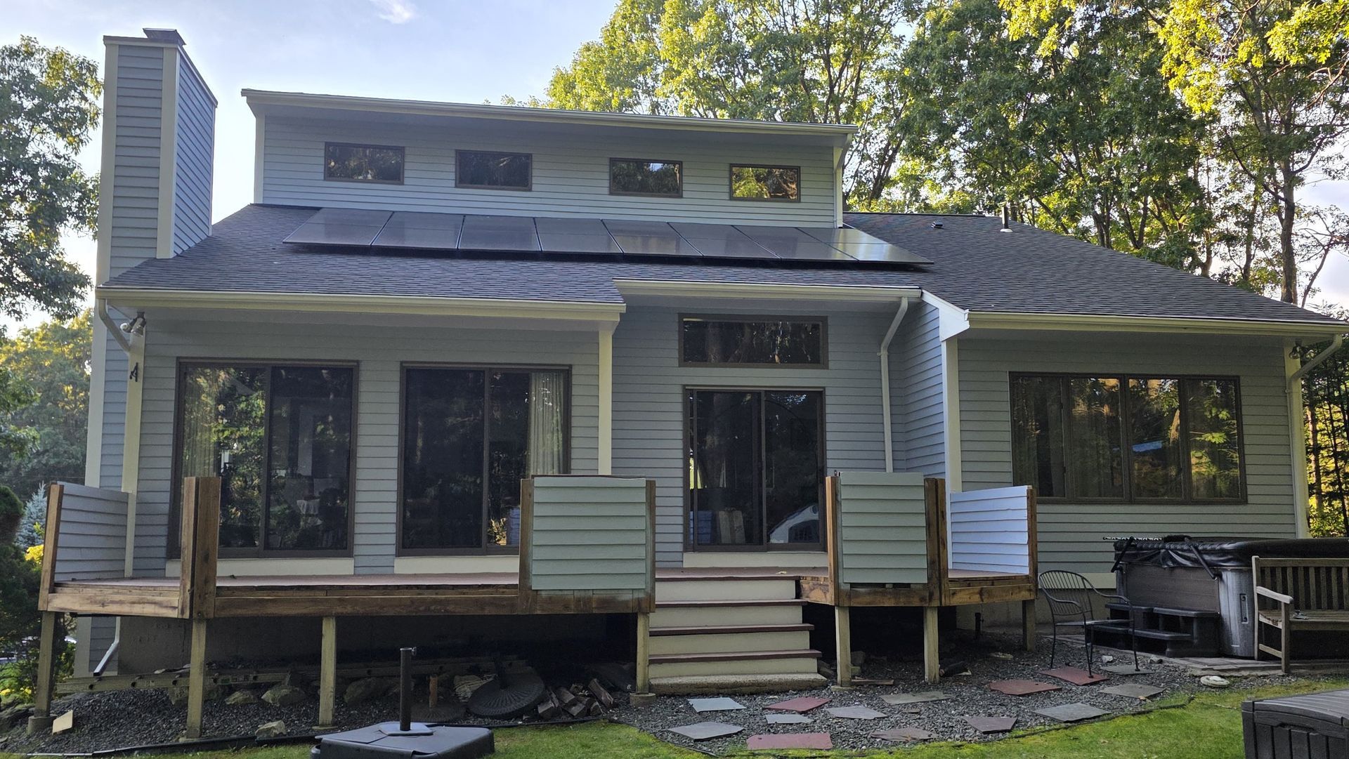 Two-story gray house with a front porch, wood steps, and a chimney surrounded by trees.