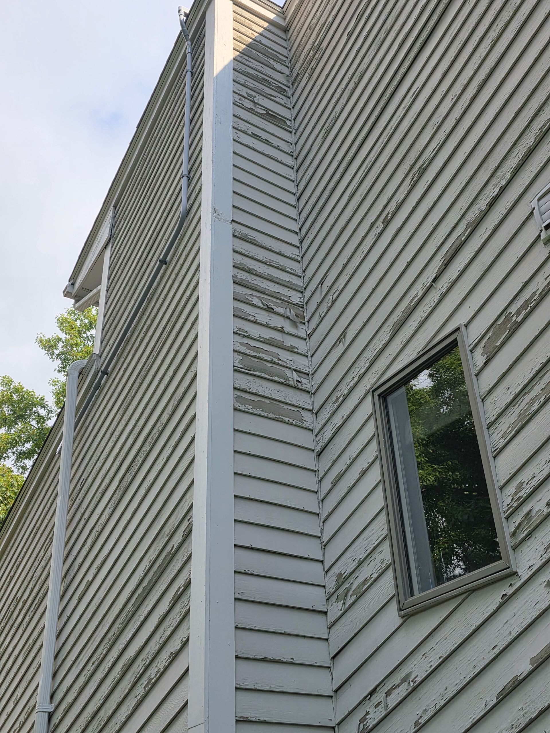 Modern gray building exterior with vertical siding and a window, viewed from below against the sky