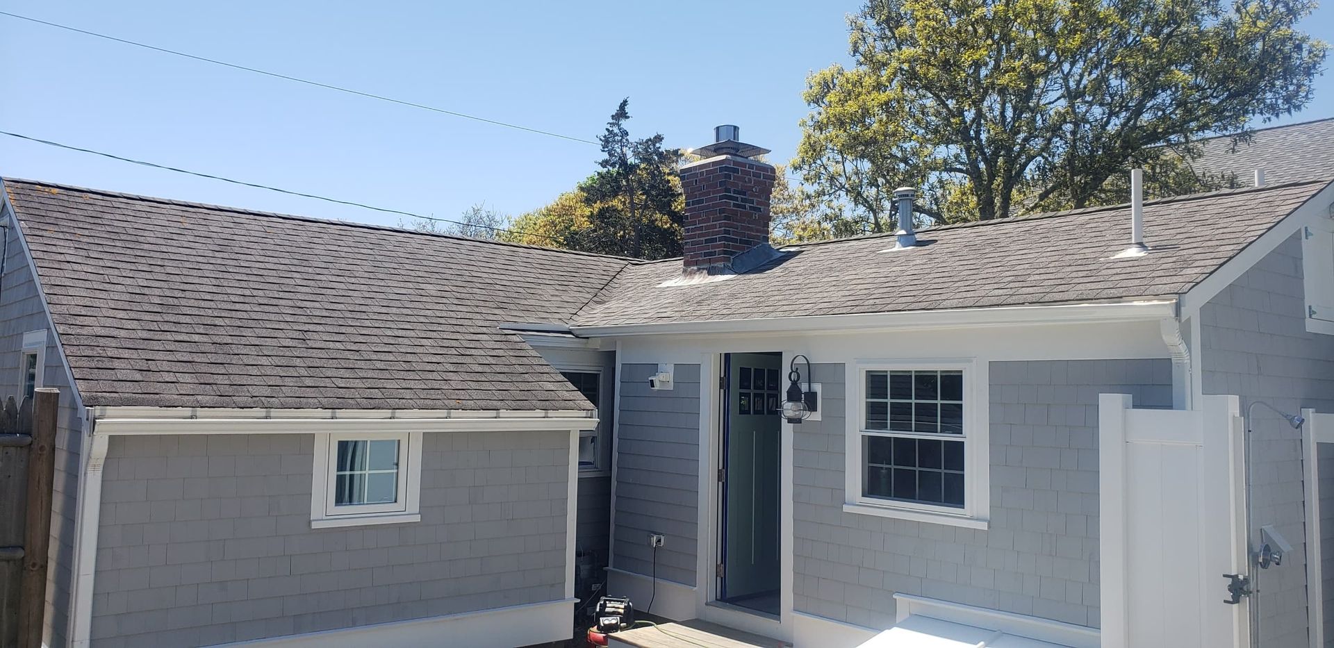 Gray house exterior with a small patio and white-trim windows under a sunny sky