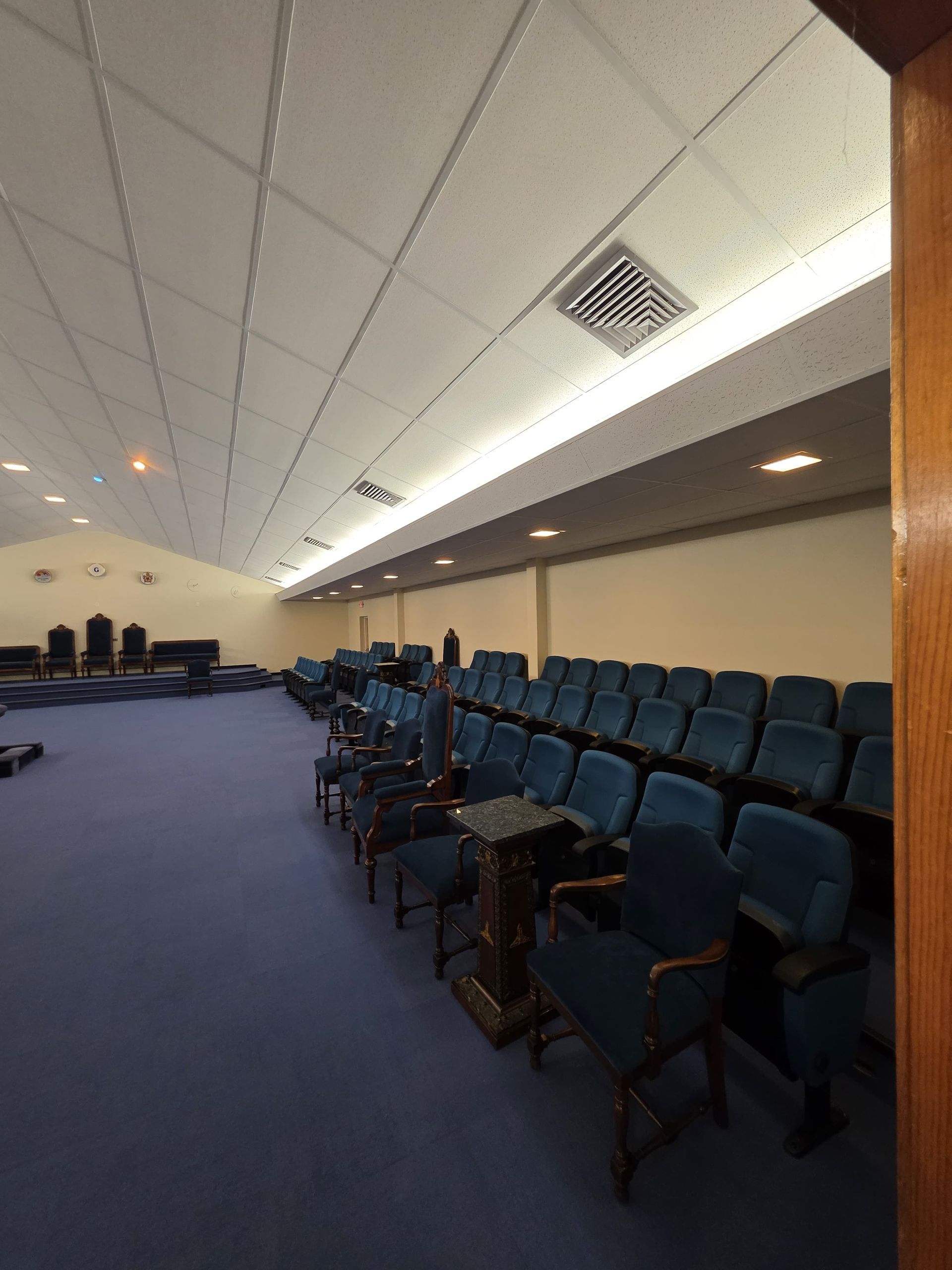 Empty auditorium with rows of blue seats and a carpeted aisle under a slanted ceiling.