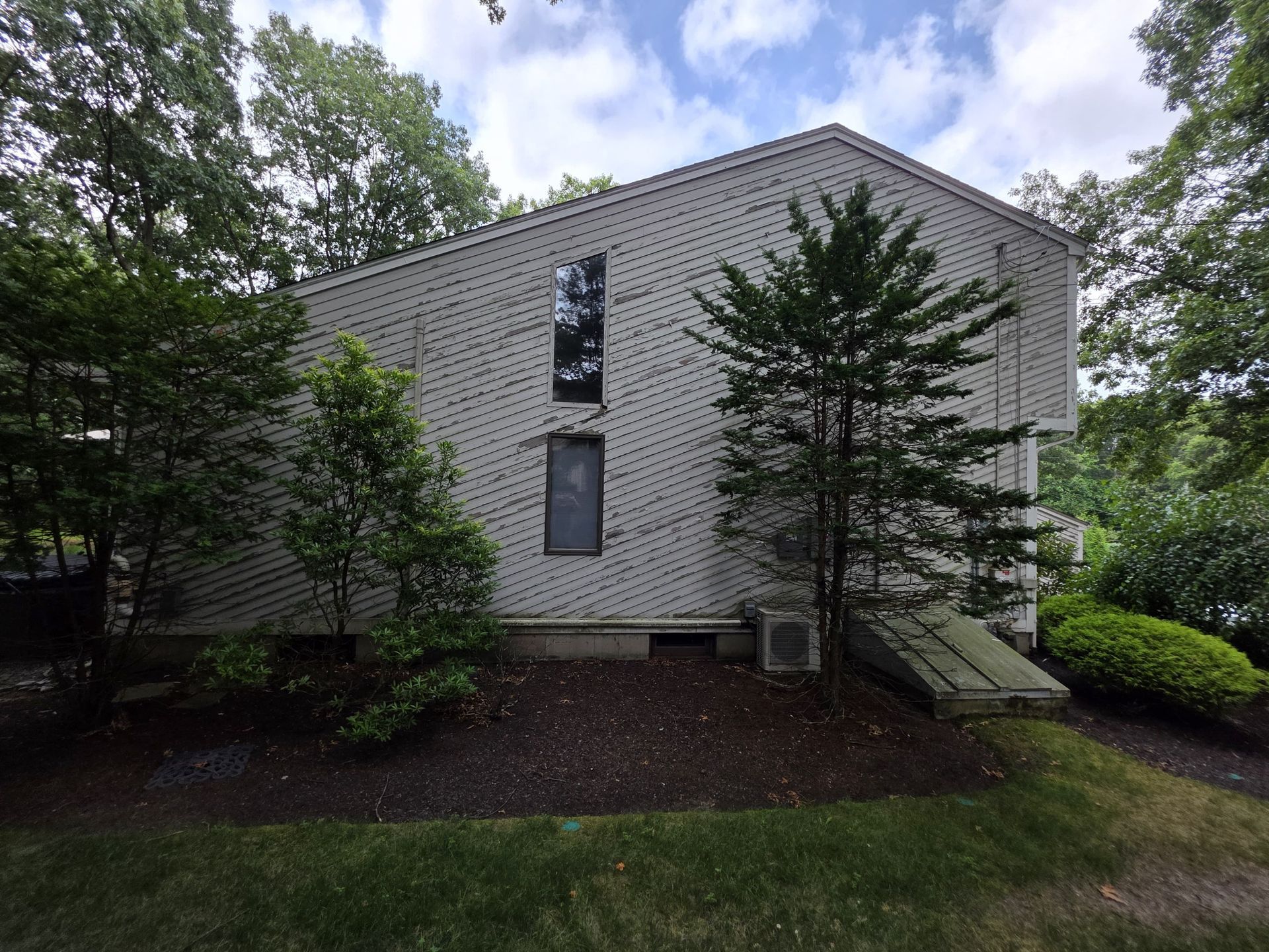 White brick apartment building with narrow windows, surrounded by trees and shrubs