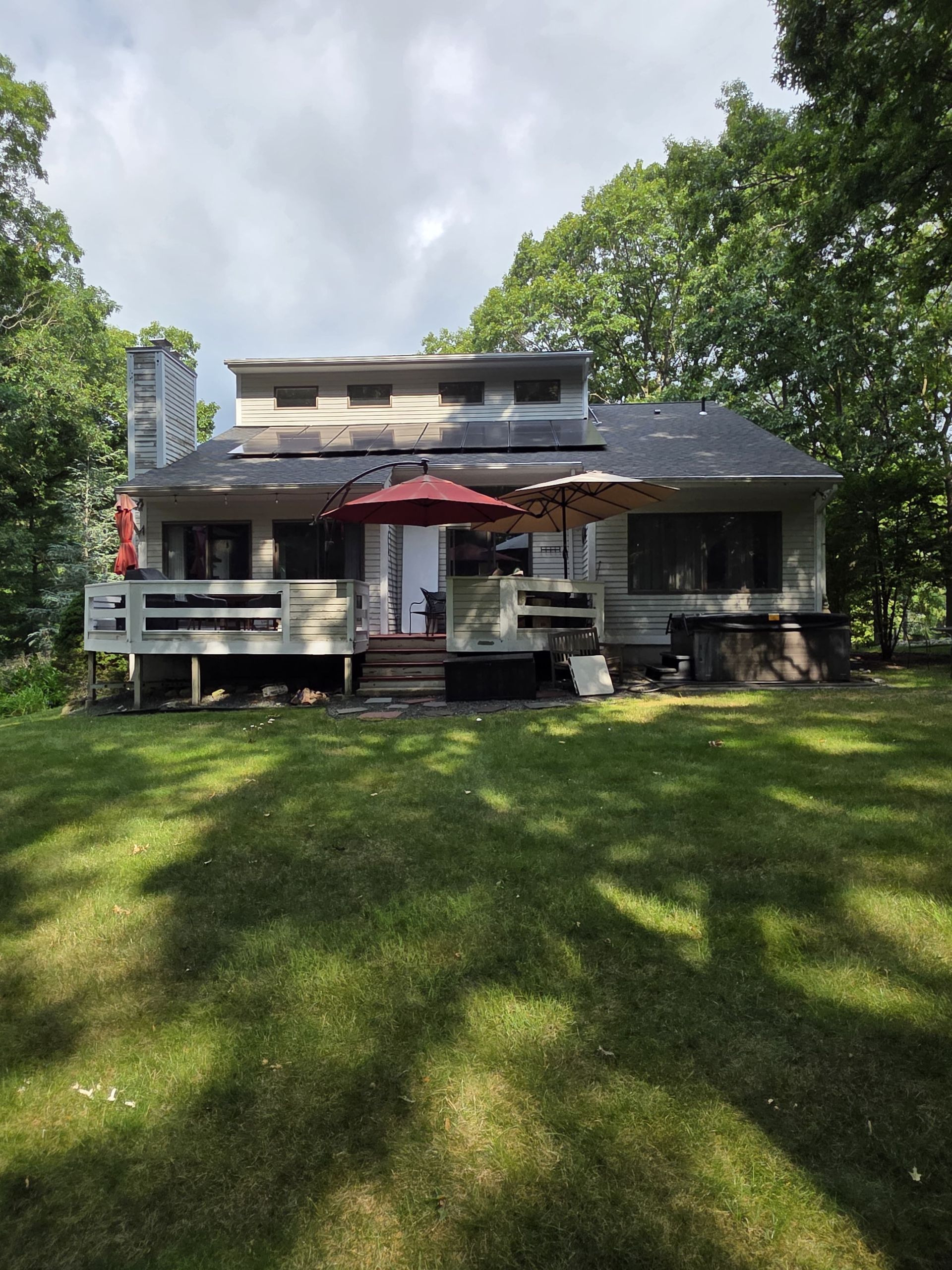 Backyard house with a wooden deck, red umbrella, and large green lawn under trees