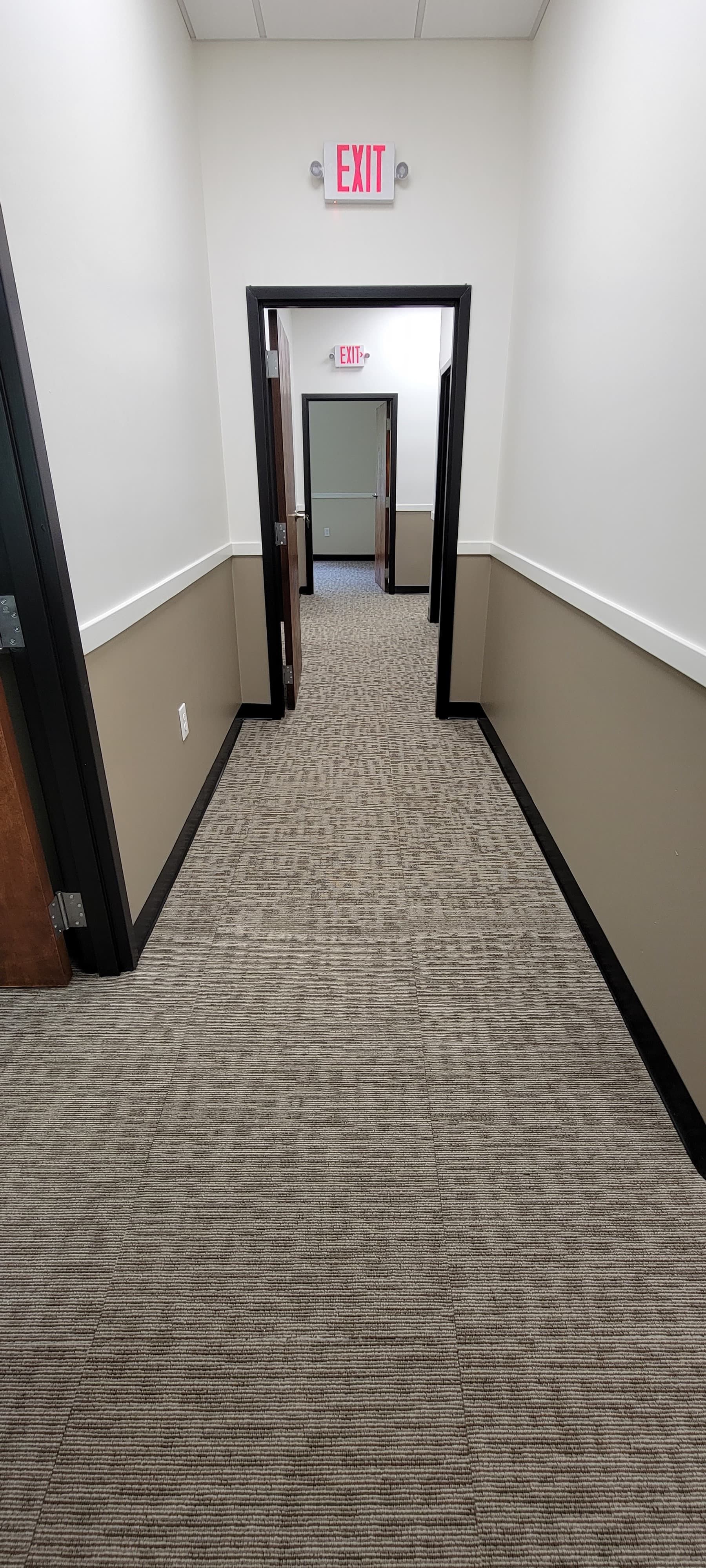 Office hallway with carpet, white walls, and red EXIT signs above doorways.