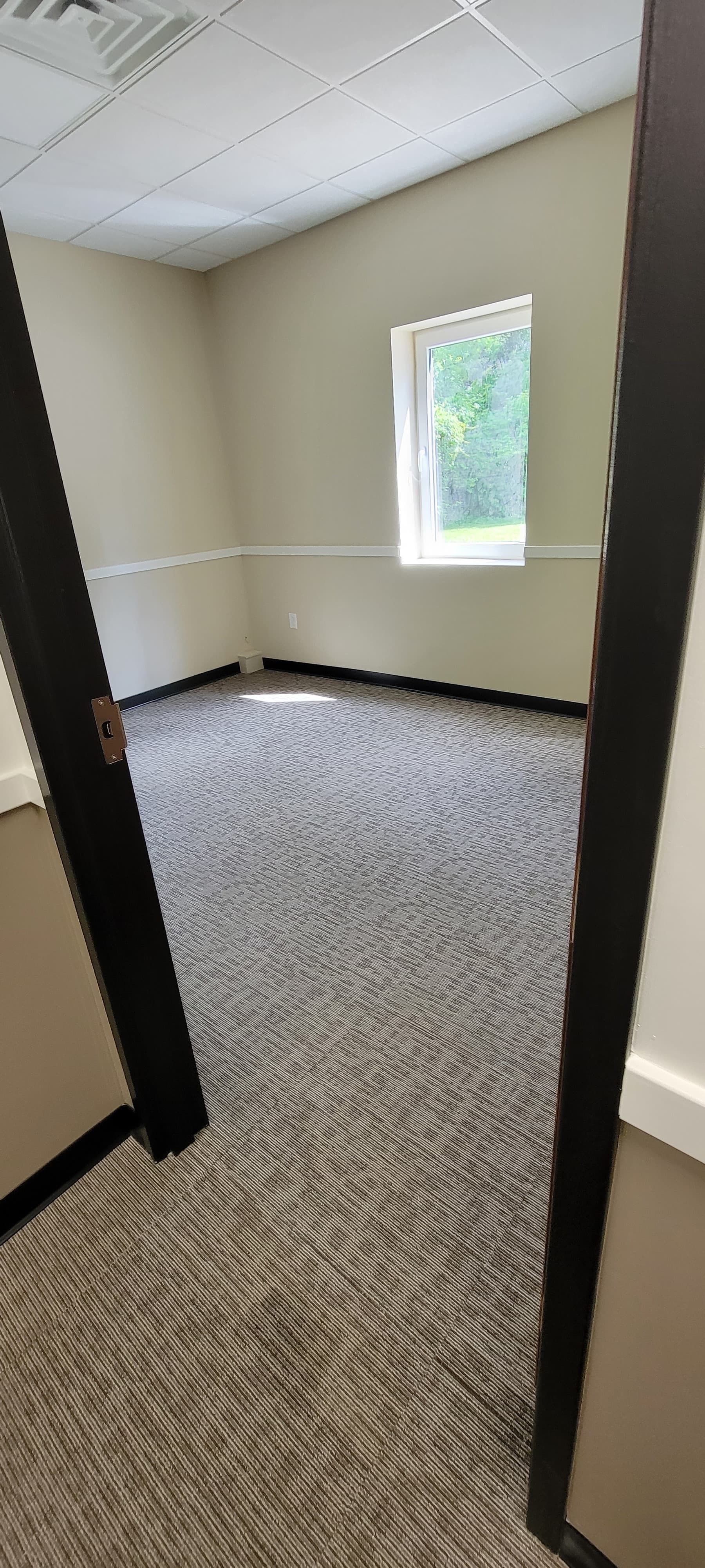 Empty office room with beige walls, patterned carpet, and a small window