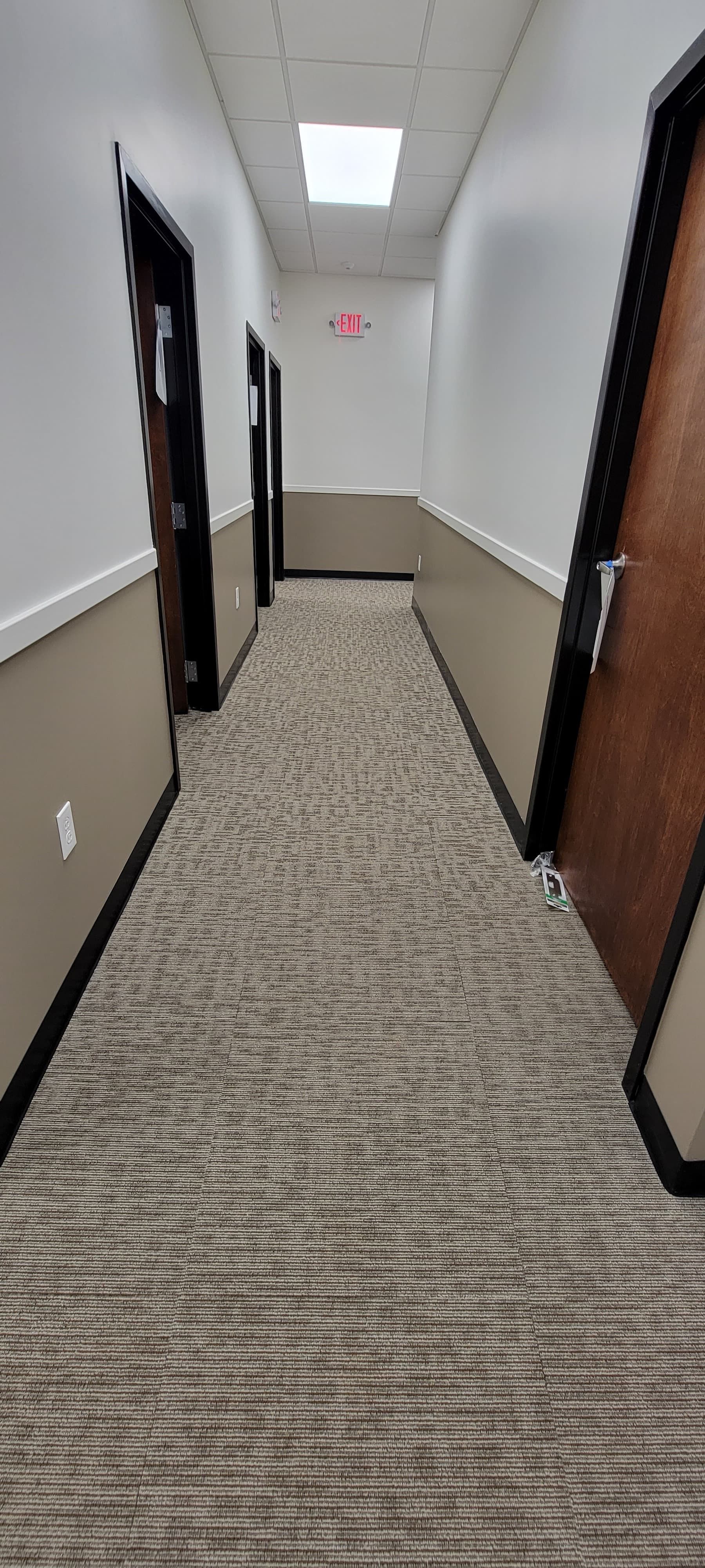 Empty office hallway with patterned carpet, beige walls, and dark wood doorways on both sides.