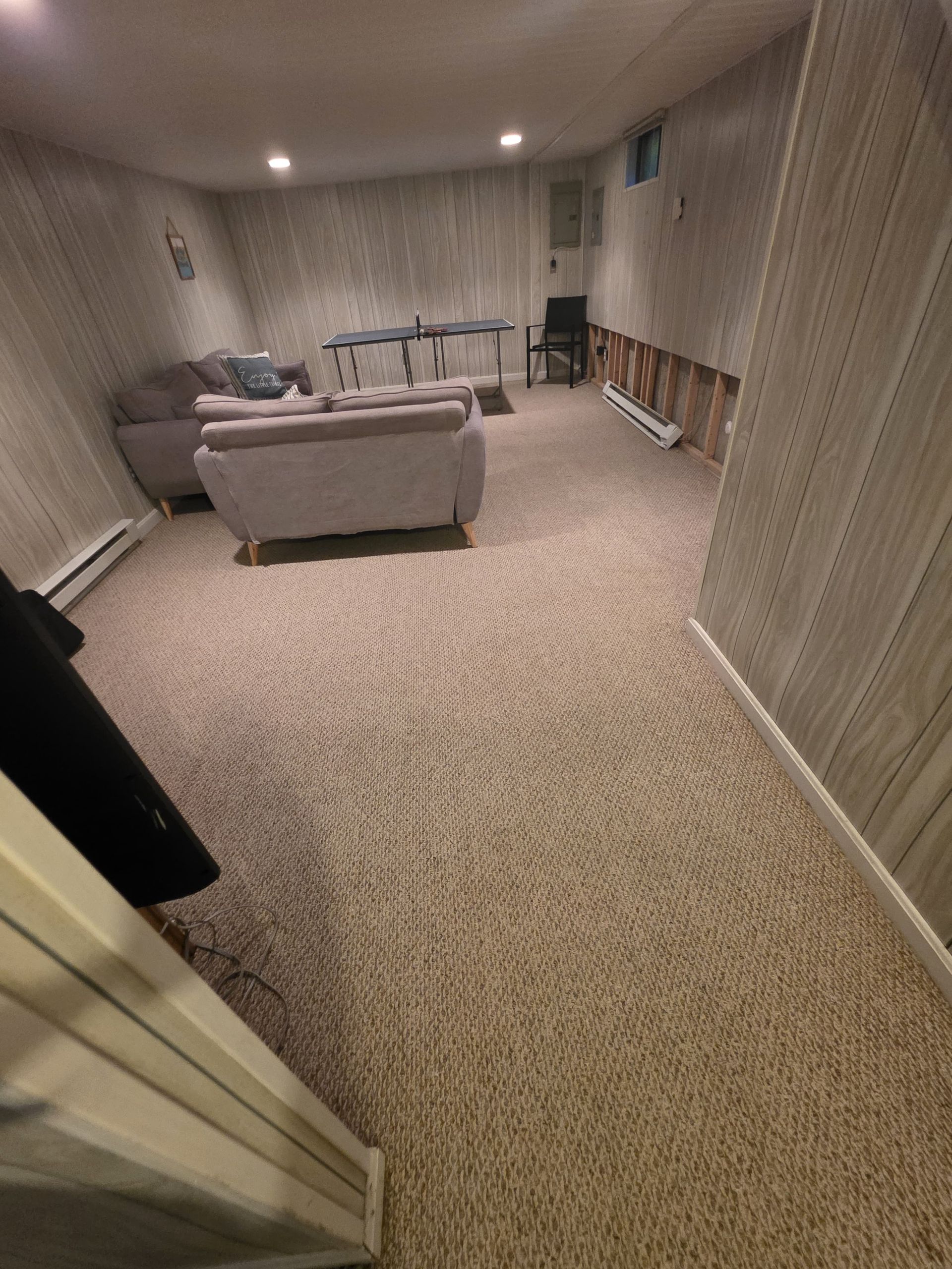 Spacious carpeted basement living room with a gray sofa, chairs, and recessed ceiling lights.