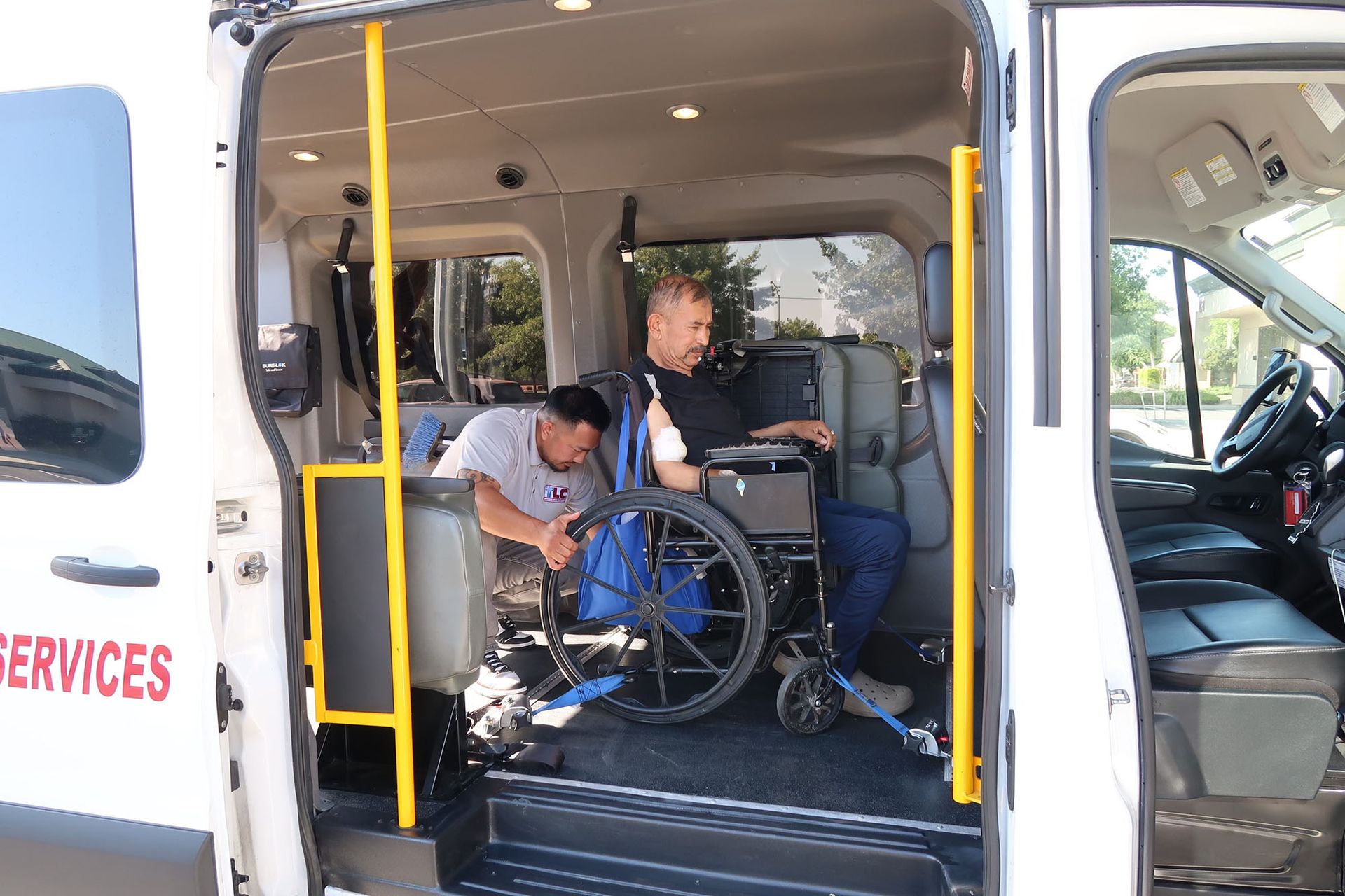 A man is helping an elderly man in a wheelchair secure his wheelchair inside the van