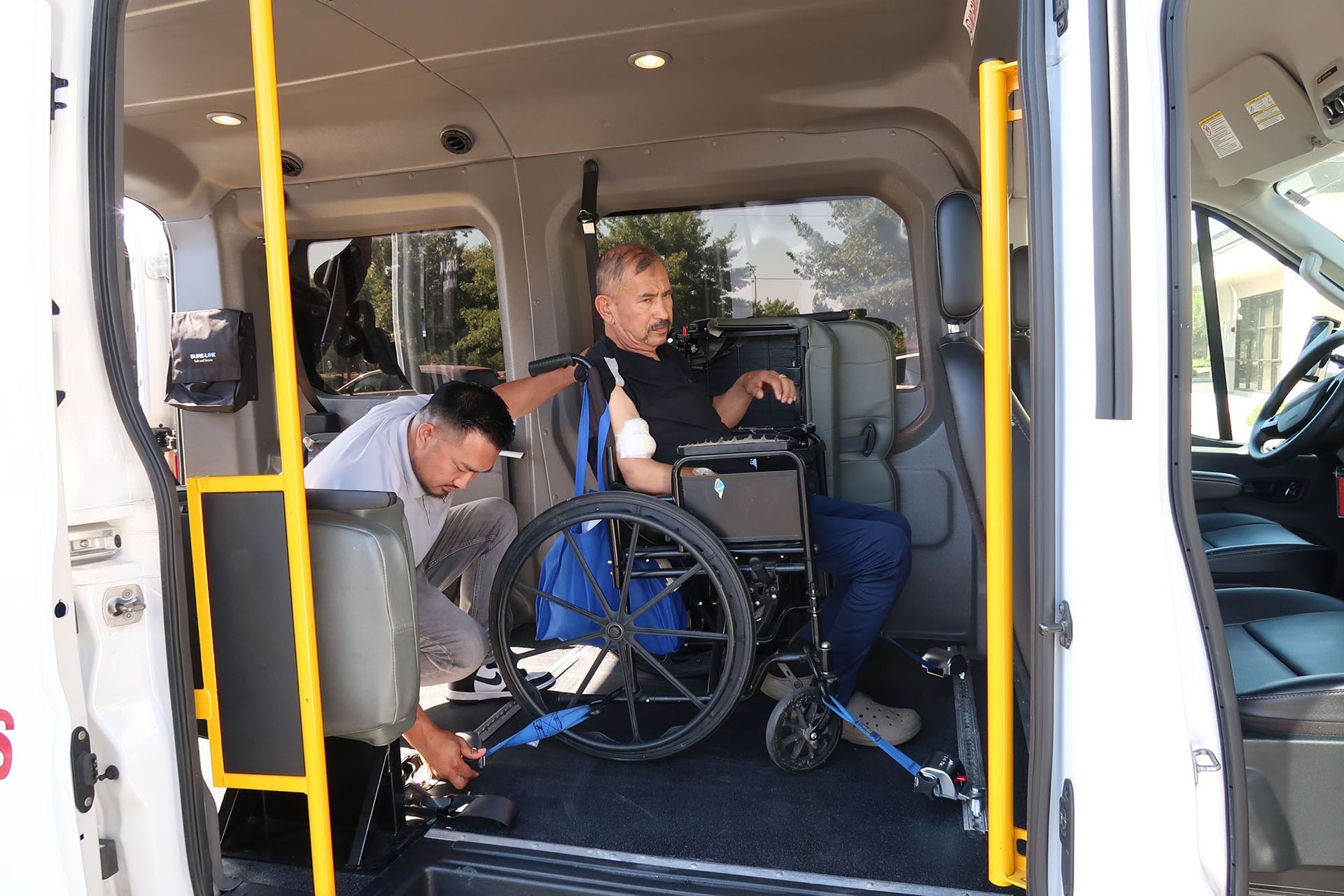 A man is helping an elderly man in a wheelchair secure his wheelchair inside the van