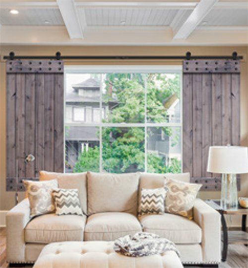 Living room with gray wooden shutters framing a large window overlooking greenery; a cream sofa with decorative pillows.