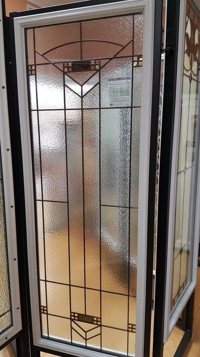 Tall window with textured glass and black geometric design, set in a white and black frame.