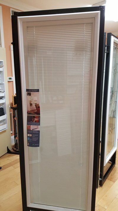 Door display with internal blinds in a showroom. White blinds, black frame.
