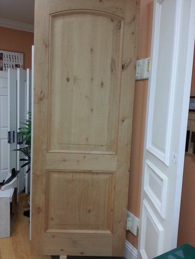 Wooden interior door with arched top panel and rectangular bottom panel, leaning against a wall.