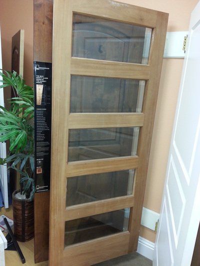 Wooden door with five glass panes, leaning against a peach-colored wall.