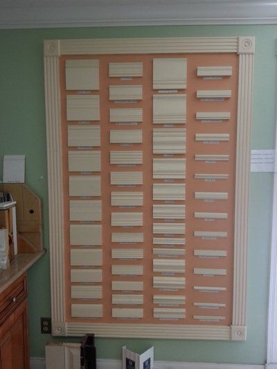 Display of molding samples on an orange board, framed in light wood, against a pale green wall.