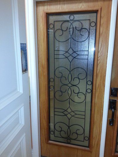 Wooden door with a decorative glass panel framed by black metalwork.