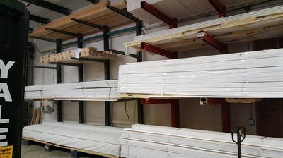 Shelving unit in warehouse holds various white trim and wood.