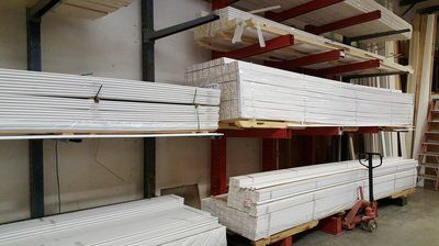 Warehouse shelving holding stacks of white molding. A pallet jack sits nearby.