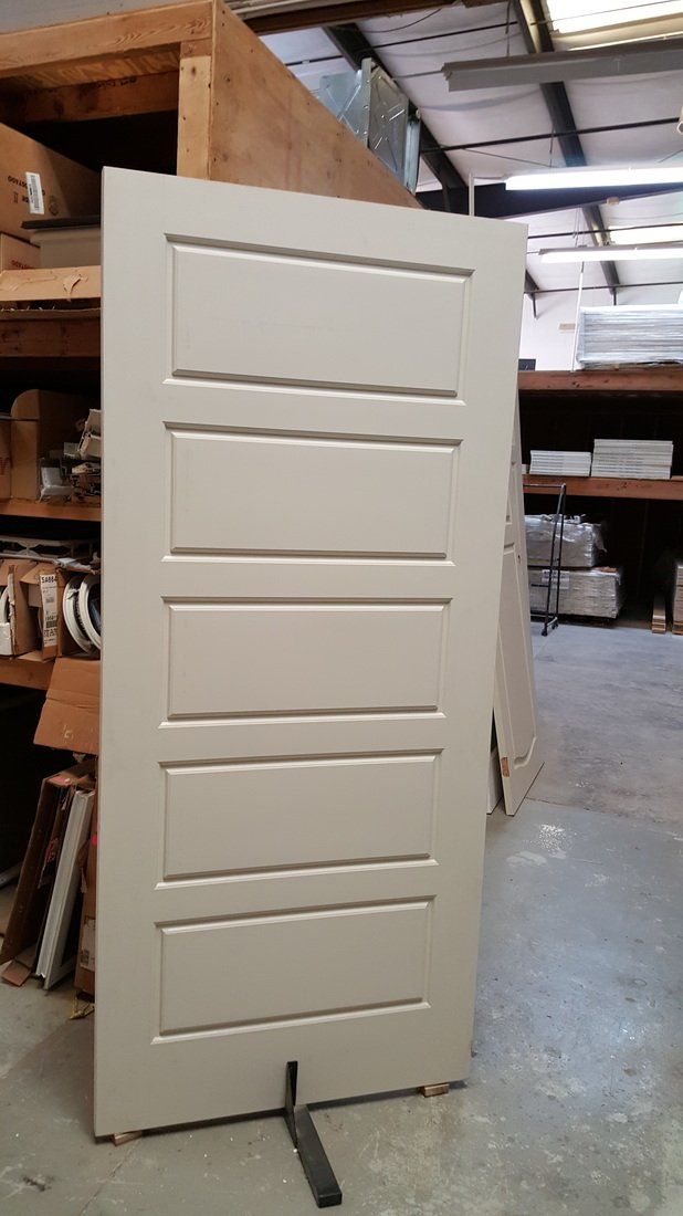 A beige four-panel interior door stands in a warehouse with wooden shelves.