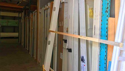 Doors stacked upright in a warehouse. White, tan, and teal shelving present.