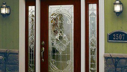 Front door with ornate glass paneling, flanked by sidelights, set in a dark wood frame.