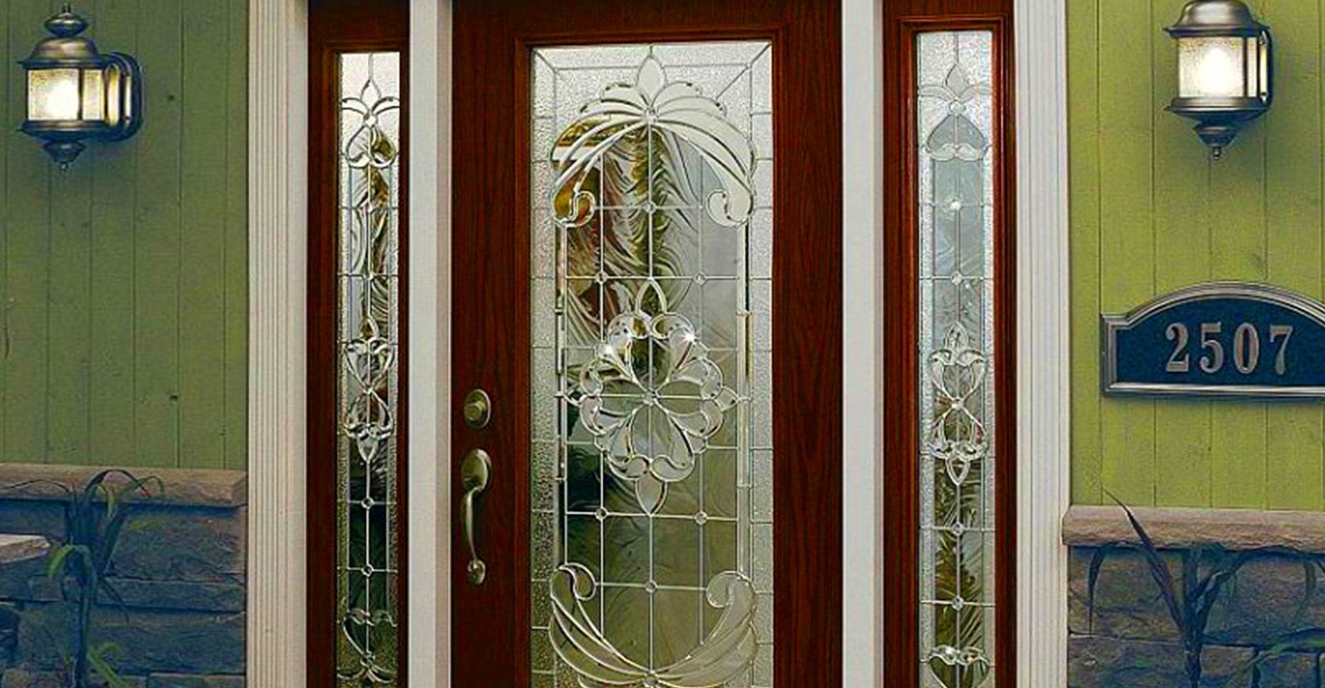 Ornate glass front door with sidelights in a brown frame, flanked by green siding, with a house number sign.