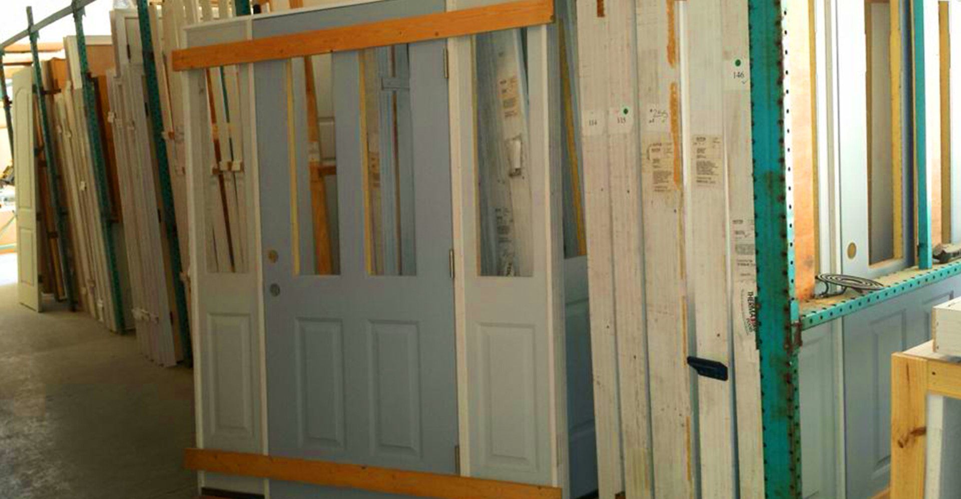 Doors of various colors and styles leaned against a rack in a warehouse.