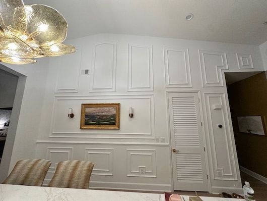 Learn More About Florida Style Trim White paneled dining room wall with framed painting, sconces, and a louvered closet door.