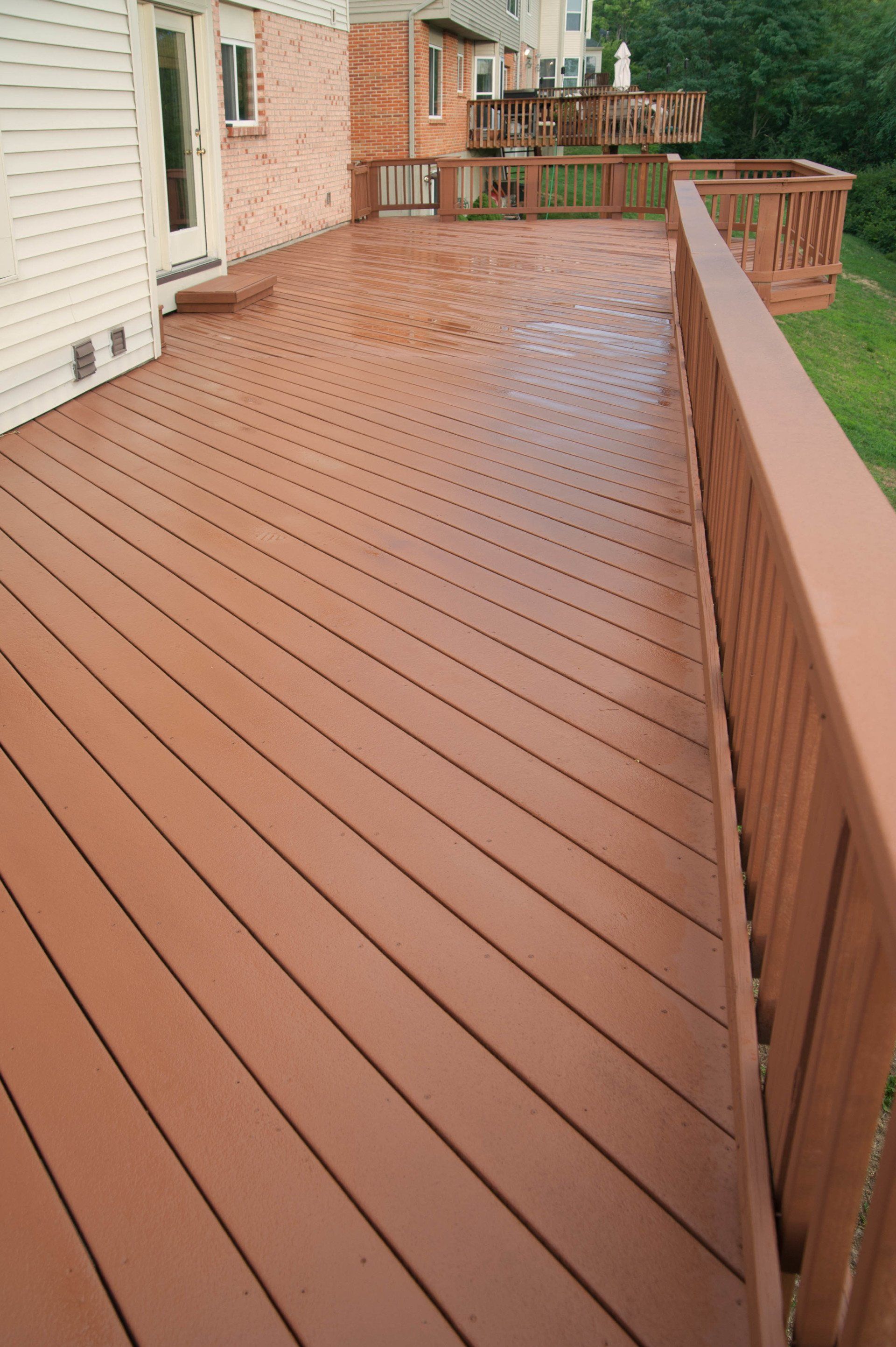 Brown wooden deck angled boards, attached to a white house, with railings and a wet surface.
