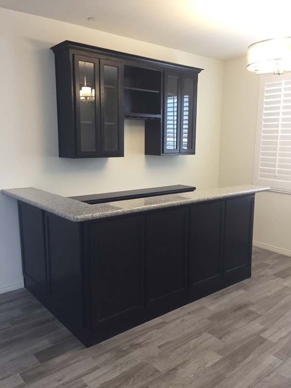 Dark wooden bar with granite countertop and matching wall cabinets in a room with light-colored walls and floor.