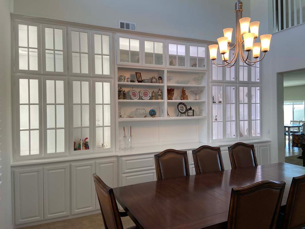 White built-in cabinetry with glass doors, a display shelf, and a dining table with chairs.