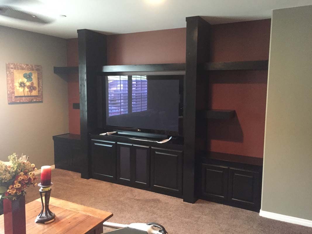 Built-in black entertainment center with TV, shelves, and cabinets on a red and gray wall.