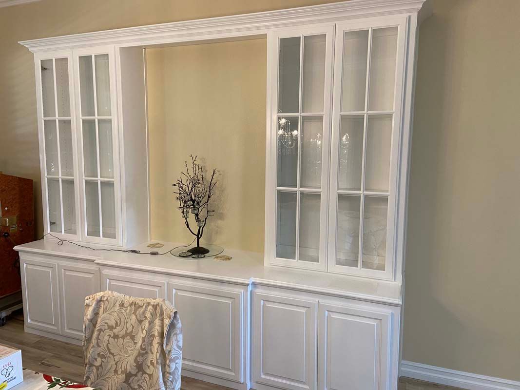 White built-in cabinet with glass doors and a central niche, against a light-yellow wall.