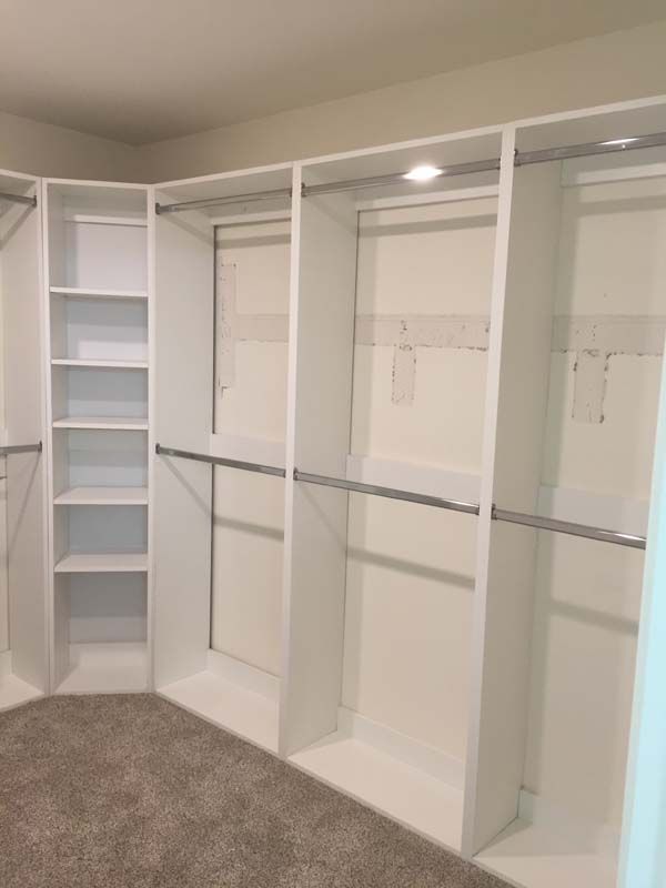 White built-in closet with shelves and hanging rods. Neutral carpeted floor, bright overhead lights.