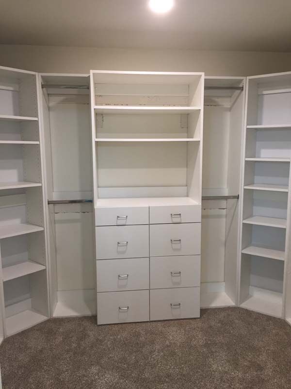 White closet organizers with shelves, drawers, and hanging rods on gray carpet.
