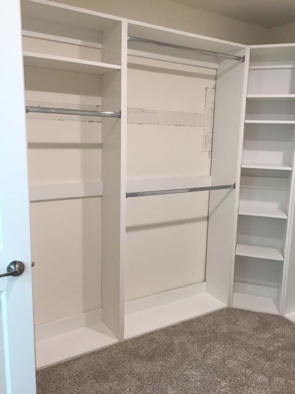White built-in closet with shelves and hanging rods; set in a room with beige carpet.