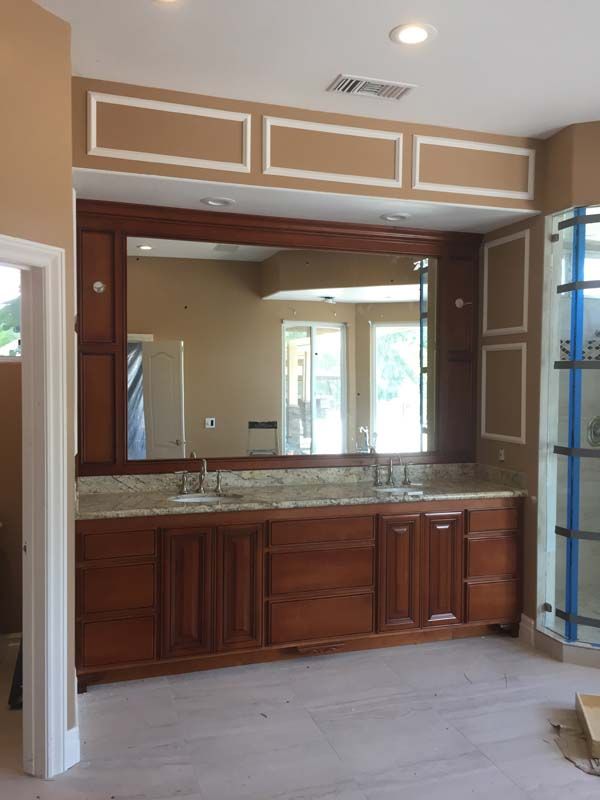 Bathroom with wooden vanity, large mirror, granite countertop, and decorative molding.