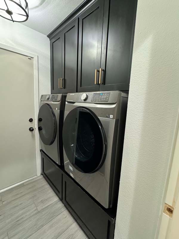 Black cabinets above a washer/dryer set in a laundry room, next to a door.