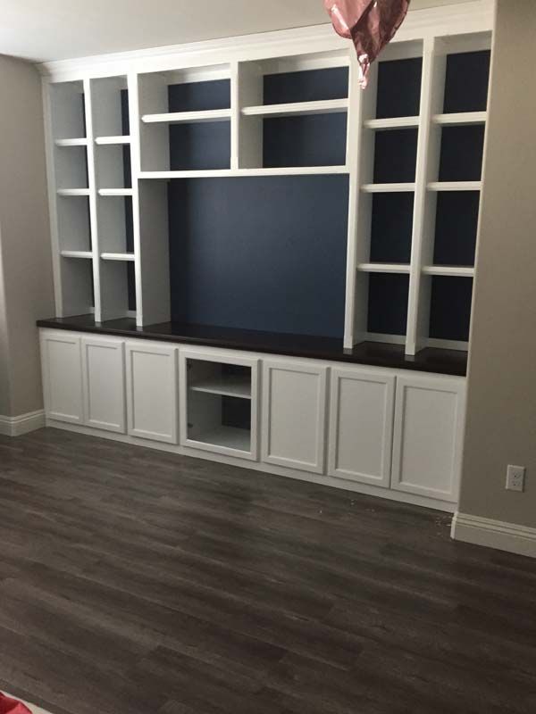 Built-in white shelves and cabinets on a dark wood floor. Dark blue backing behind shelves, and a gray wall.