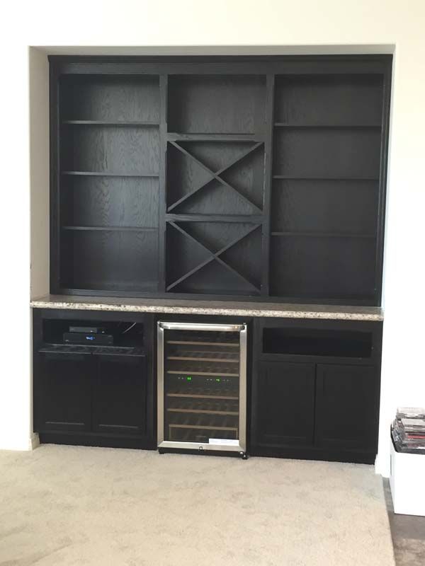 Black built-in cabinet with bookshelves, wine rack, wine fridge, and lower cabinets. Granite countertop.
