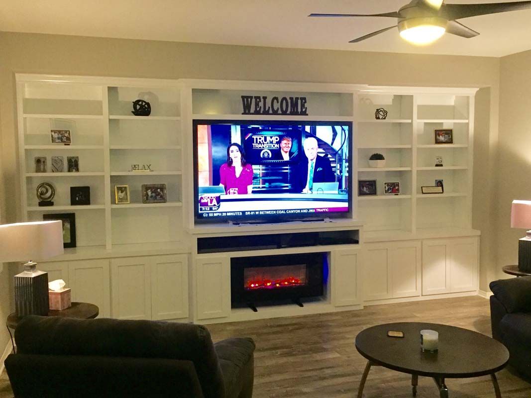 Living room with built-in white shelving, TV, fireplace, and decor. Includes dark furniture, and a round coffee table.