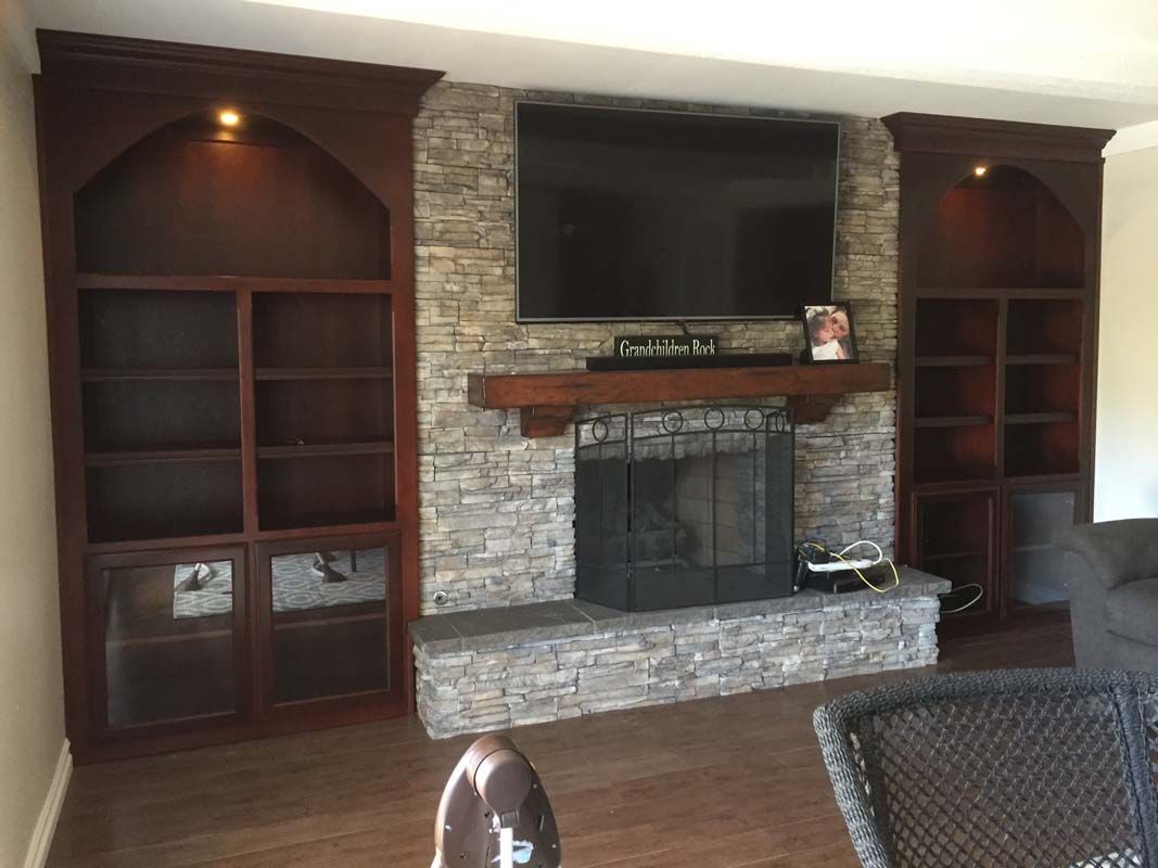 Fireplace with stone surround, TV, built-in bookshelves, and wooden mantel in a room.