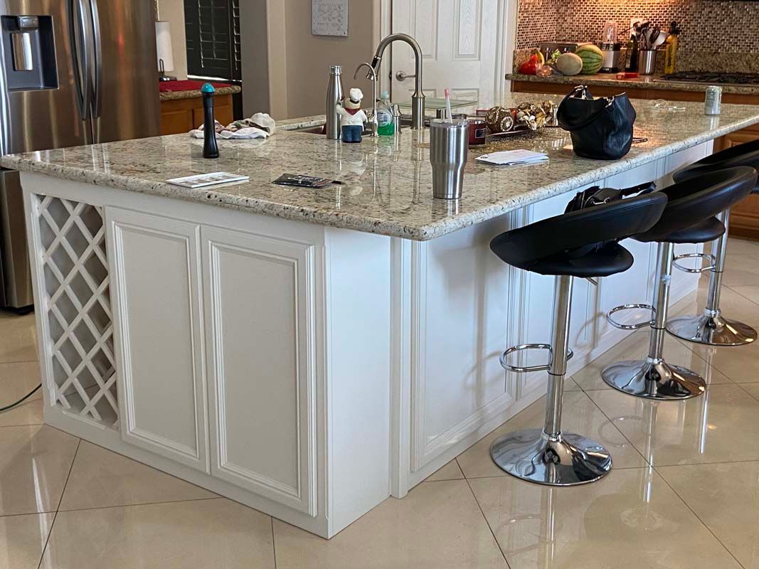 Kitchen island with white cabinets, granite countertop, chrome stools, and a wine rack.
