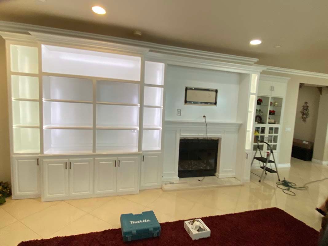 Built-in white cabinets with shelves, fireplace, and red rug in a room. A tool box sits on the floor.