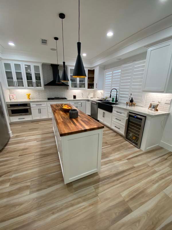 Modern kitchen with white cabinets, wood island, and black pendant lights.