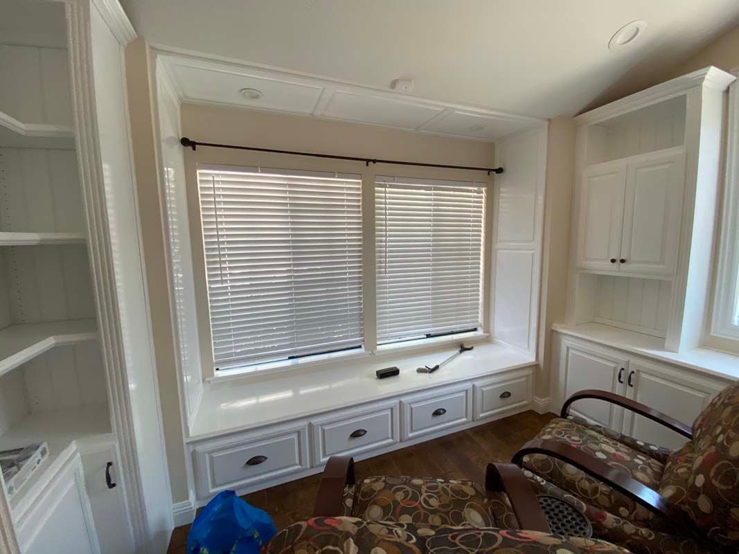 Built-in window seat with drawers and blinds, flanked by white cabinetry. A floral armchair sits nearby.