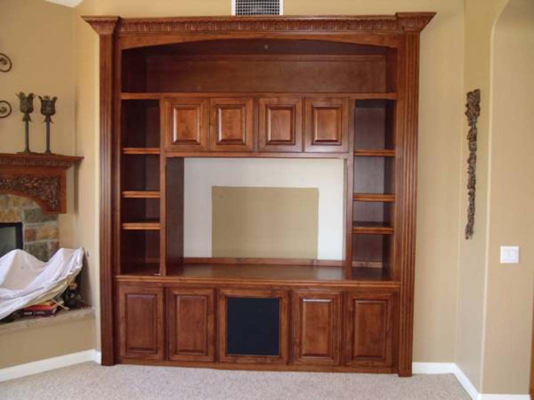 Dark wood built-in entertainment center with cabinets, shelves, and a center space for a TV in a room with beige walls.