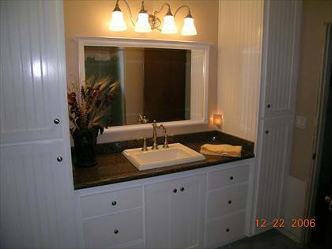 Bathroom with a white vanity, sink, and mirror. White cabinets flank the vanity, with dark countertop.