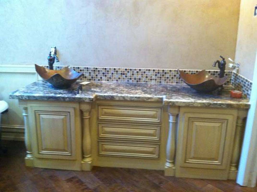 Vanity with two copper bowl sinks, wood cabinets, granite countertop, and tile backsplash.