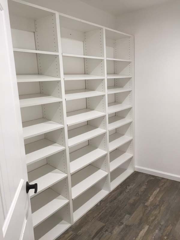 White built-in bookshelves against a white wall and dark wood-look flooring. A black doorknob is on the left.